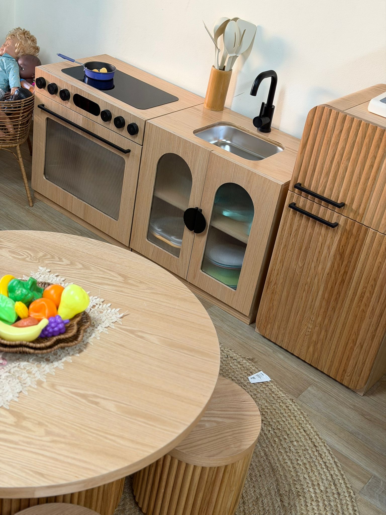 Indoor early learning environment showcasing a child-sized wooden play oven, sink unit, and a bowl of toy fruit