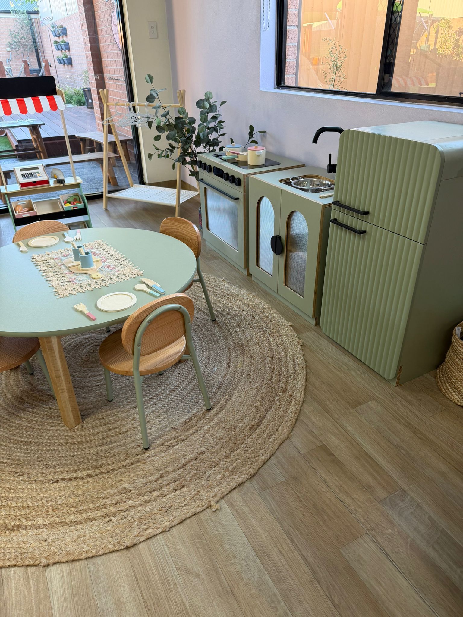 Early learning classroom environment showcasing a small wooden dining table set, a large jute rug, and a toy kitchen