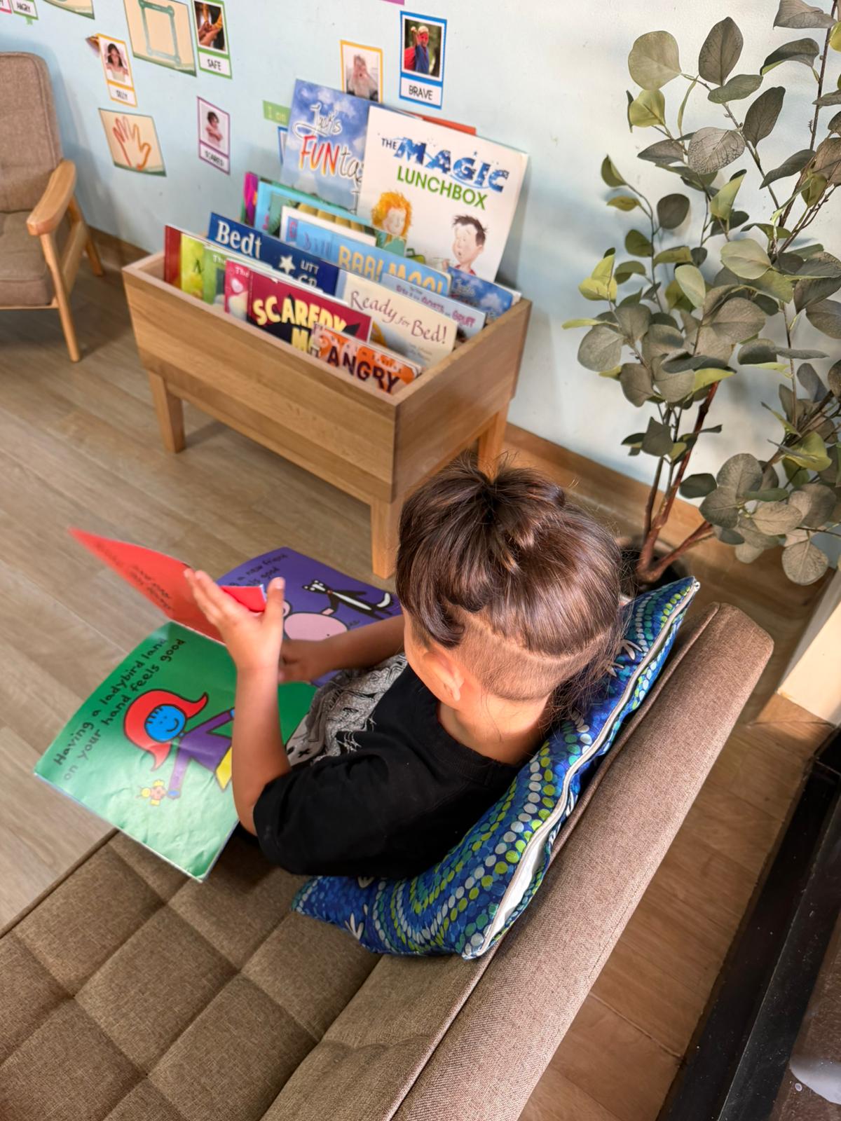 Preschool child sitting comfortably on a soft floor cushion looking intently at an open colorful picture book
